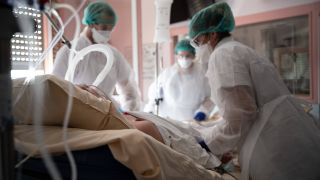 Medizinpersonal in Spezialkleidung an Krankenbett auf Intensivstation (Bild: imago images/Hans Lucas)