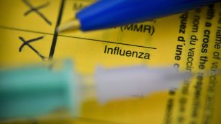 Impfpass mit Schrift Influenza unter Spritze und Stift (Bild: imago images/Schöning)