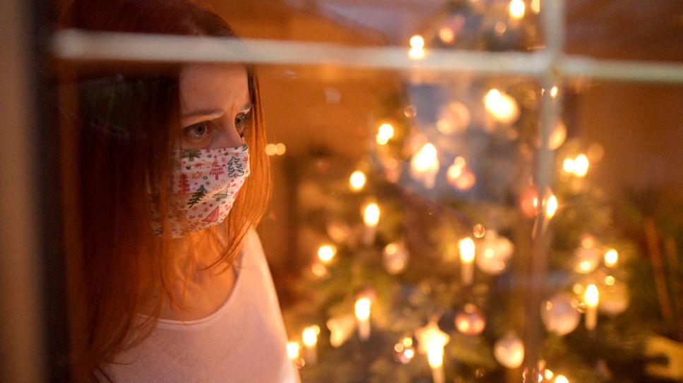 Eine Frau mit Mund-Nasenschutz-Maske schaut sehnsüchtig aus dem Wohnzimmerfenster (Quelle: imago/MiS)