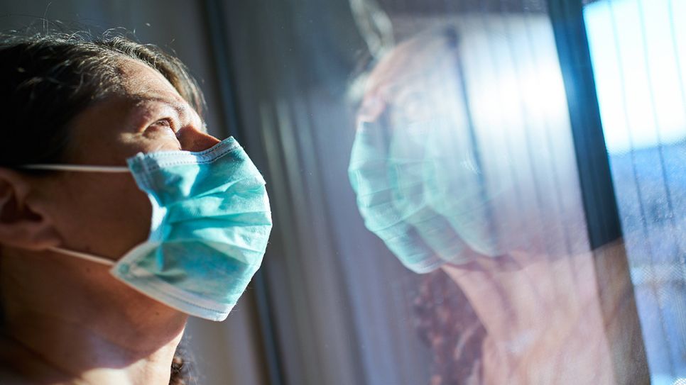 Frau mit Mund-Nase-Schutz steht am Fenster (Bild: imago images/Action Pictures)