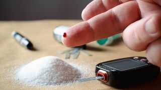 Hand mit Einstichstelle vor Zucker, Teststreifen und Diabetesmessegerät auf Tisch (Bild: imago images/CTK Photo)