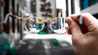 Brille in einer Hand vor Stadtkulisse (Bild: unsplash/Josh Calabrese)
