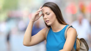 Frau fasst sich in Fußgängerzone schmerzverzerrt an Kopf (Bild: Colourbox)