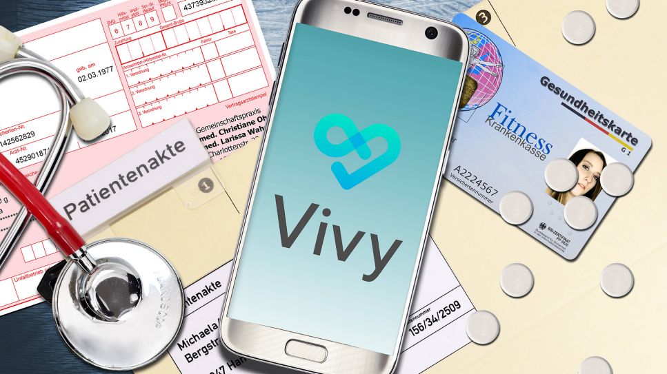 Vivy App auf Handy neben Patientenakten und Chipkarte (Bild: imago/Christian Ohde)