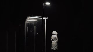 Person in weißem Mantel steht nachts unter Lampe an Bushaltestelle (Bild: unsplash/Patrik Laszlo)