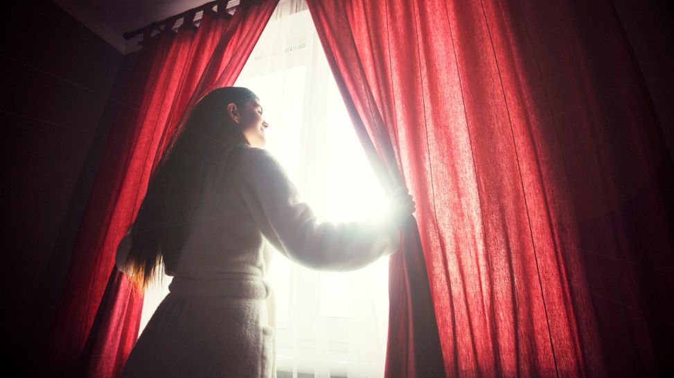 Frau blickt aus Fenster in die Morgensonne (Quelle: colourbox)