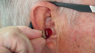 Älterer Mann hält In-Ear-Hörgerät an Gehörgang (Bild: unsplash/Mark Paton)