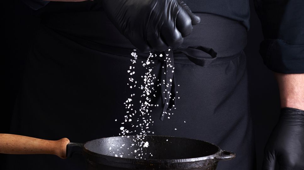 Hand eines Kochs streut Salz in eine Pfanne (Bild: imago/Panthermedia)