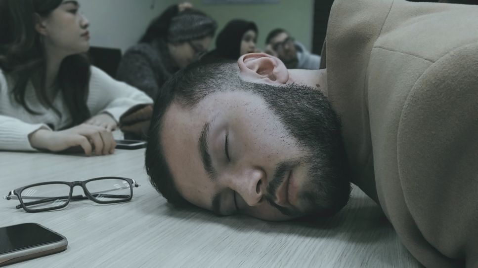 Narkolepsie: Mann schläft auf Tisch bei Bürobesprechung (Bild: unsplash/Abdulbosit Melikuziev)