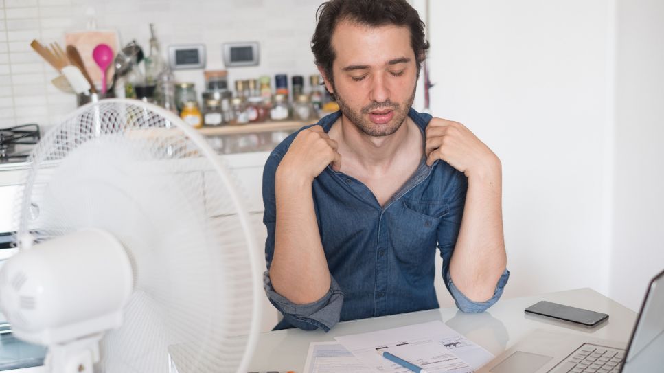 Hitzestress zuhause: Mann sitzt schwitzend vor Ventilator an Küchentisch (Bild: imago/agefotostock)