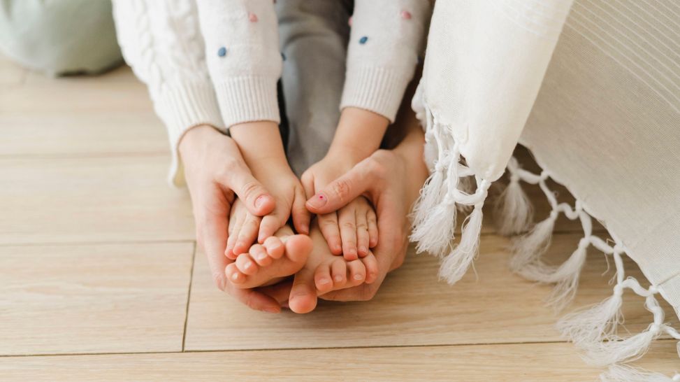 Hand-Mund-Fuß-Krankheit Symbolbild: Frau hält mit ihren Händen ihre Füße und die Hände ihrer Tochter (Quelle: imago/Westend61)