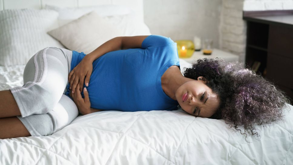 Bauchschmerzen: Frau mit Bauchschmerzen liegt auf Bett (Bild: imago/Shotshop)