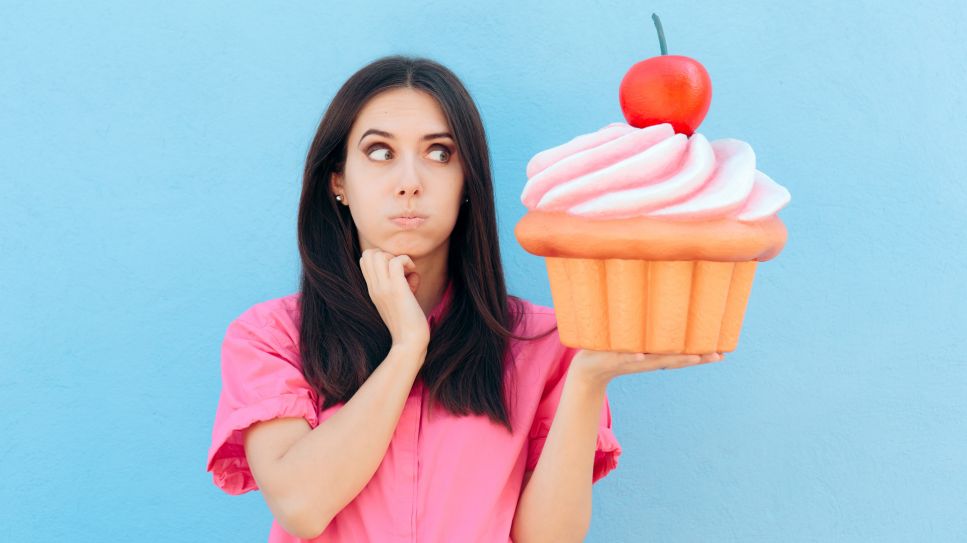 Heisshunger überwinden: Bild zeigt Frau, die einen riesigen Muffin auf der Hand hält und ihn fragend anschaut (Quelle: colourbox)