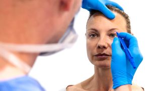 Augenlidstraffung: Bild zeigt Gesicht einer Frau, der ein Arzt am Auge Markierungen für eine OP setzt (Bild: imago images/Cavan Images)