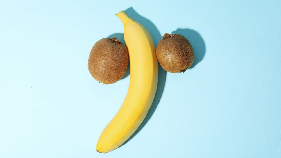 Penisverkrümmung: Bild zeigt Banane und 2 Kiwis links und rechts davon auf blauem Tisch (Bild: Colourbox)