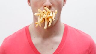 Binge Eating, Bild zeigt Mann: Der Mund steckt voll mit Pommes (Quelle: Colourbox)