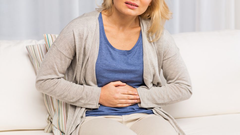 Bauchschmerzen, Bild zeigt Frau, die auf dem Sofa sitzt und sich den Bauch vor Schmerzen hält (Quelle: Colourbox)