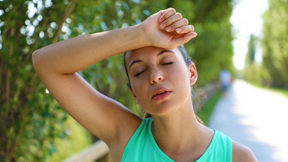 Sonnenstich: Frau draußen in Hitze legt Arm auf Stirn (Bild: imago images/YAY Images)