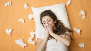 Symptom Schnupfen: Frau niest in Taschentuch, umgeben von benutzten Taschentüchern auf Bett (Bild: Colourbox)