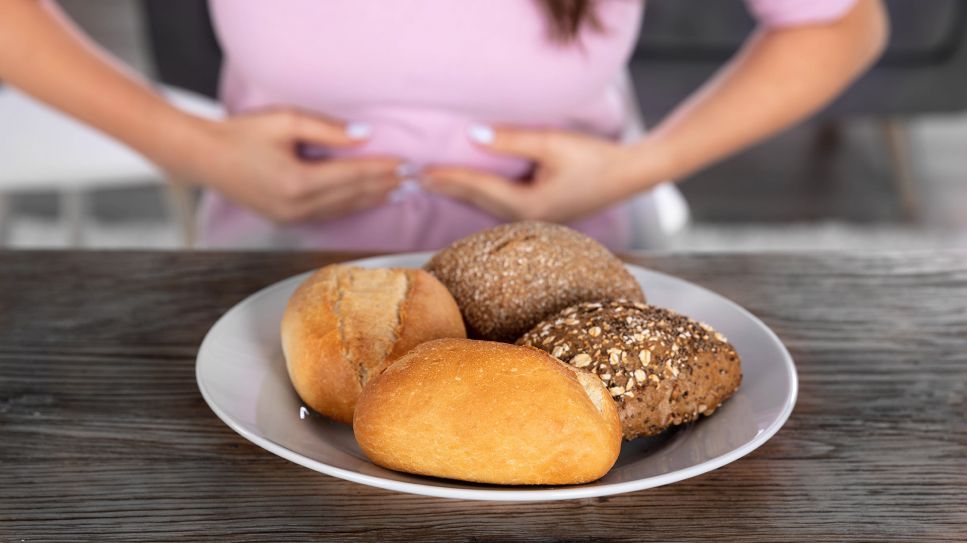 Medikament gegen Glutenunverträglichkeit: Bild zeigt Teller mit Brötchen vor Frau mit schmerzendem Bauch (Bild: Imago Images/Panthermedia)