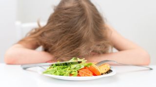 Blutdruckabfall nach dem Essen: Bild zeigt Mädchen mit Kopf auf Tisch vor einem Teller mit Essen (Bild: Colourbox)