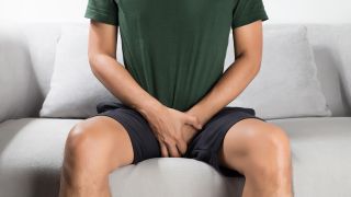Prostata-Früherkennung: Bild zeigt Mann auf Couch, der Hände zwischen Beine klemmt (Bild: Colourbox)