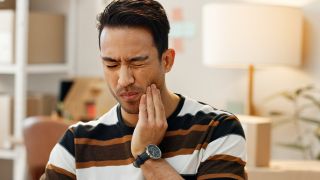 Zähneknirschen: Mann mit schmerzendem Kiefer hält sich Hand an Wange (Bild: Colourbox)