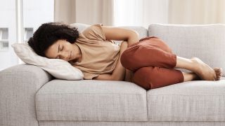 Endometriose diagnostizieren: Bild zeigt Frau schmerzgekrümmt auf Sofa liegend (Bild: Colourbox)