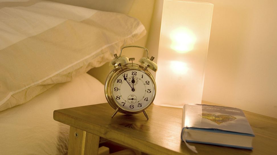 Wecker und Buch liegen auf einem Nachttisch (Quelle: imago/blickwinkel)
