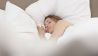 Eine Frau schläft zugedeckt in ihrem Bett (Quelle: imago/Westend61)