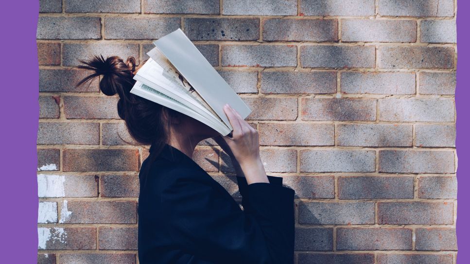 Eine junge Frau verdeckt ihren Kopf mit einem Buch (Quelle: unsplash/Siora18)