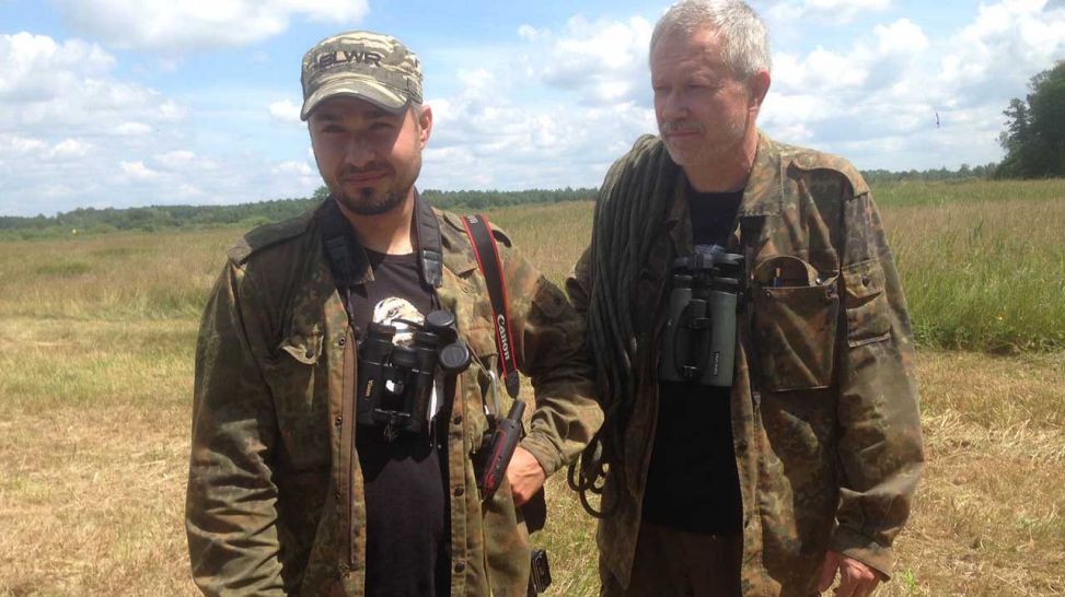 Zwei Männer - Sylwester Aftyka und  Janusz Wojciak mit Kameraausrüstung stehen auf dem Feld; Quelle: rbb/Maren Schibilsky
