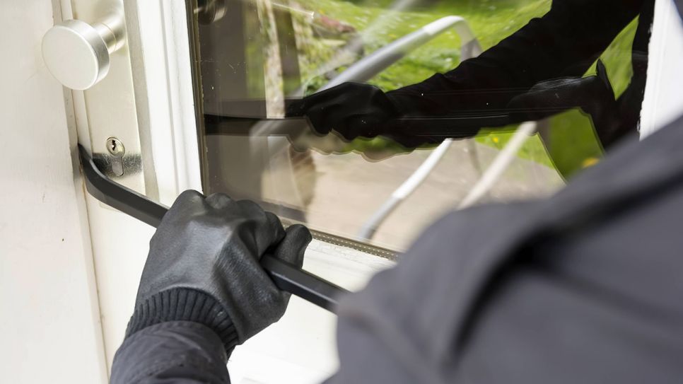 Ein Mann bricht mit einer Brechstange eine Haustür auf (Quelle: imago images/Westend61)