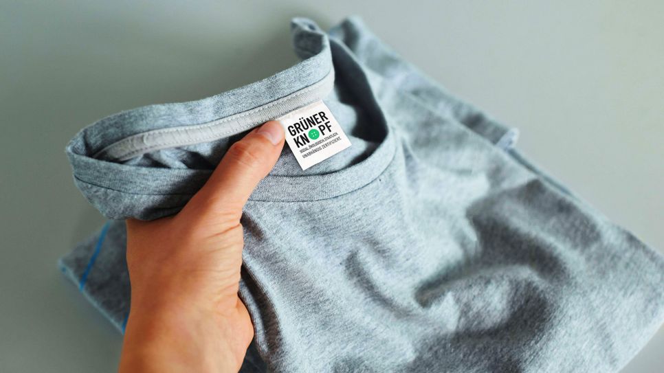 Ein graues T-Shirt mit dem Label "Grüner Knopf" wird von einer Hand hochgehoben (Quelle: BMZ)