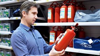 Ein Mann steht in einem Laden vor einem Regal mit Feuerlöschern und sieht sich einen Feuerlöscher genauer an (Quelle: Colourbox)