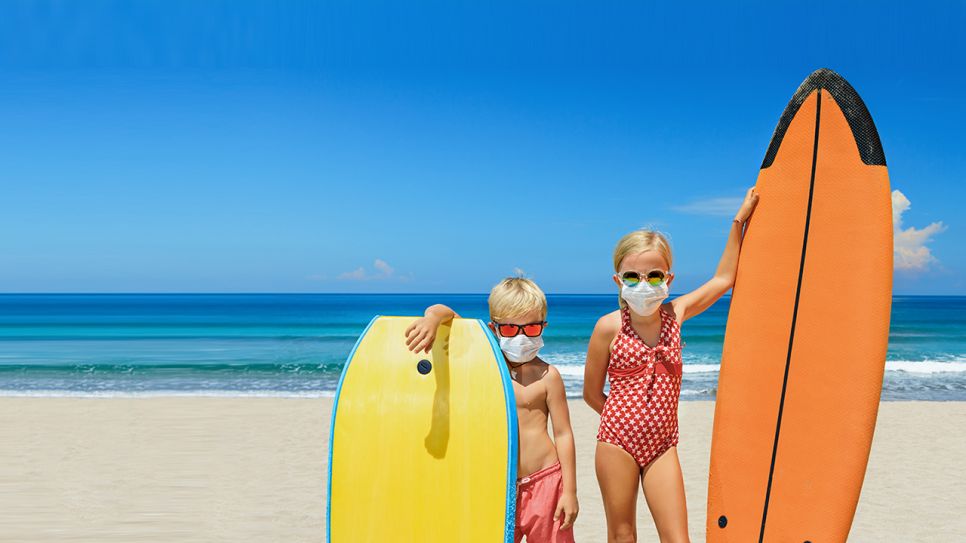 Symbolbild für Urlaub und Urlaubsplanung in Coronazeiten: Kinder mit Maske und Surfbrettern am Strand (Quelle: Colourbox)