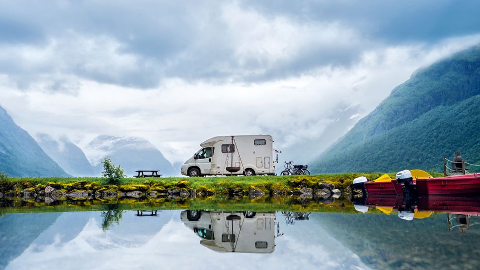 Wohnmobil steht an einem See mit Bergen im Hintergrund. Quelle: COLOURBOX