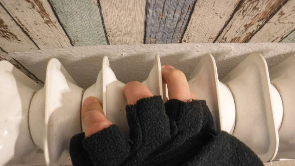 Eine Hand mit Handschuh an einer Heizung. Quelle: imago images