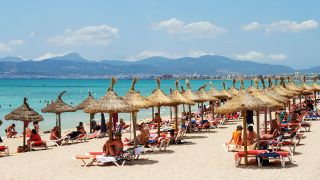 Strand an der Playa de Palma und Bucht von Palma im Sommer mit Urlaubern, die unter Sonnenschirmen liegen (Quelle: IMAGO / Chris Emil Janßen)