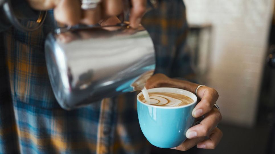 Ein Barista gießt Milch in einen Cappuccino (Quelle: imago images/Zoonar)