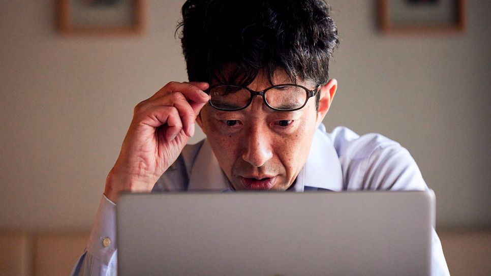 Ein Mann schaut ungläubig auf den Bildschirm seines Laptops (Quelle: imago images/AFLO)