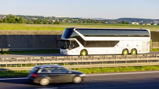Ein weißer Reisebus fährt auf einer Autobahn, in die andere Fahrtrichtung fährt ein schwarzer PKW (Quelle: IMAGO / Arnulf Hettrich)