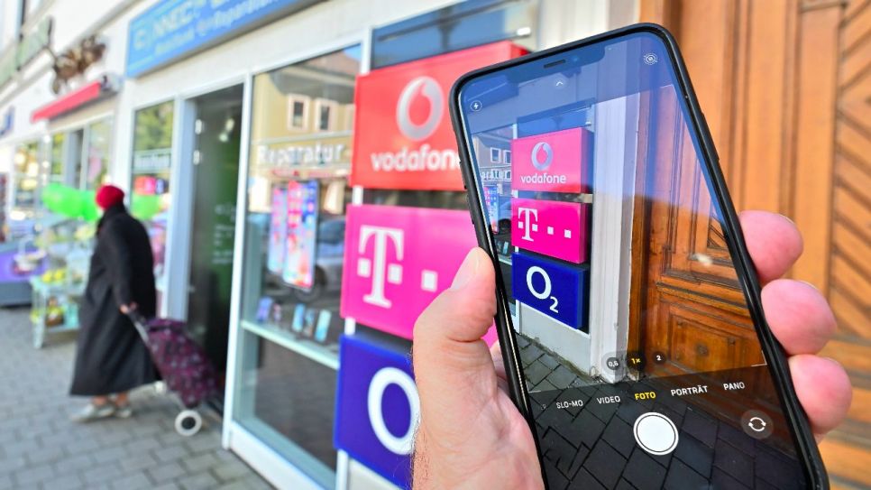 Smartphone in der Hand vorm Telekommunikations-Geschäft (Quelle: imago images/Rolf Poss)
