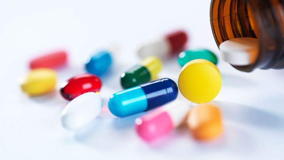 Verschiedene Tabletten und Kapseln in unterschiedlichen Farben liegen neben einem umgekippten braunem Tablettenglas auf einem weißen Untergrund (Quelle: IMAGO / Westend61)