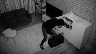 Ein Einbrecher ist auf dem Bild einer Überwachungskamera dabei zu sehen, wie er Schränke in einem Wohnzimmer durchsucht (Quelle: IMAGO / Panthermedia)