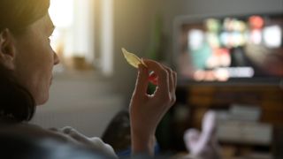Frau mit Chips in der Hand vorm Fernseher (Quelle: imago images/Pond5 Images)