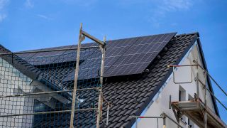 Aunfahme einer Baustelle mit einem Baugerüst, das um ein Einfamilienhaus herum steht; Solarpanele auf dem Dach (Quelle: IMAGO / MiS)