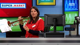 Supermarkt-Moderatorin Janna Falkenstein sitzt hinter einer eingeblendeten Supermarkt-Kasse und spielt Trompete (Quelle: rbb)