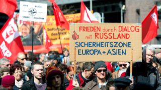 Demonstranten nehmen am 04.04.2015 in Berlin am Ostermarsch unter dem Motto «Die Waffen nieder» teil, organisiert von der Friedenskoordination. Sie führen u.a. ein Banner mit der Aufschrift "Frieden durch Dialog mit Russland - Sicherheitszone Europa + Asien" mit sich. (Quelle: Maurizio Gambarini/dpa)