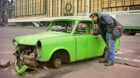 Ein Passant schaut sich im Januar 1991 einen schrottreifen grünen Trabi an, der vor dem Palast der Republik in Berlin abgestellt wurde. (Quelle: dpa/Wolfgang Kumm)